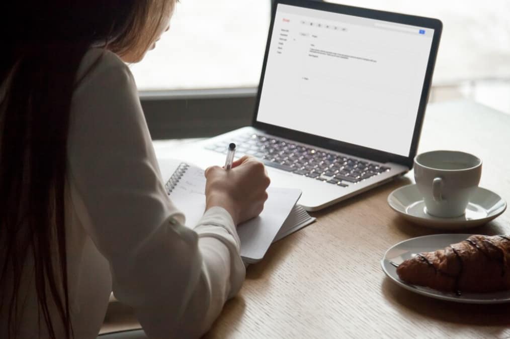 A person writing beside an open laptop