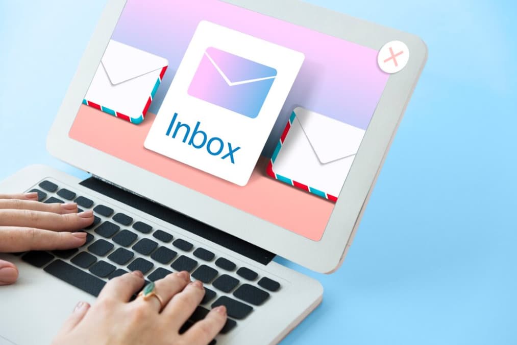 Hands typing on a laptop with colorful email inbox icons on the screen